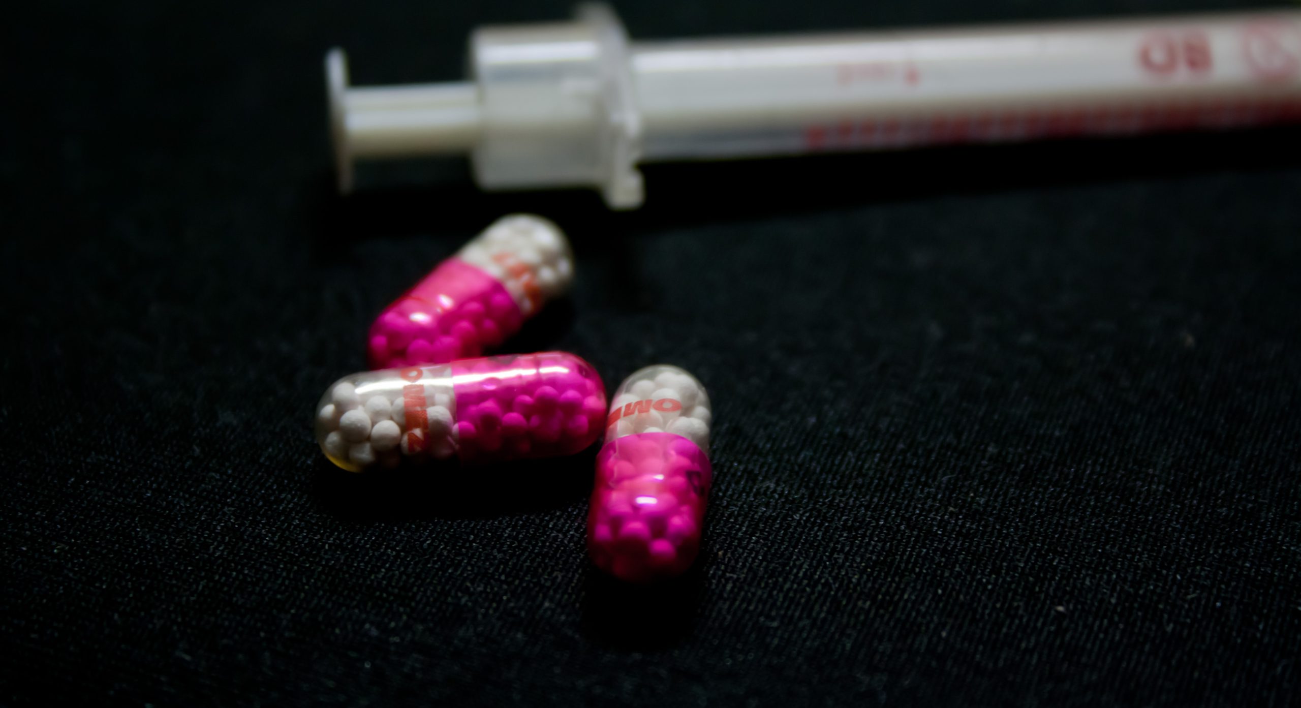 Close up of bright pink and white capsules, out-of-focus needle in background on a black surface