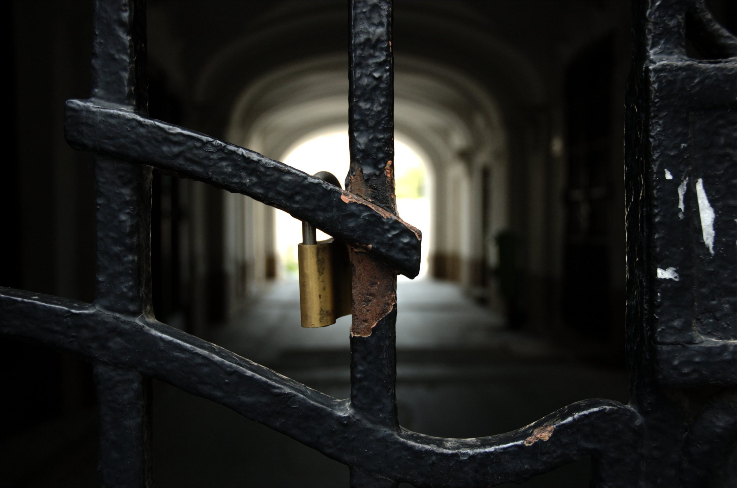 Close up of rusty locked black gate bars with distant light seen through a tunnel