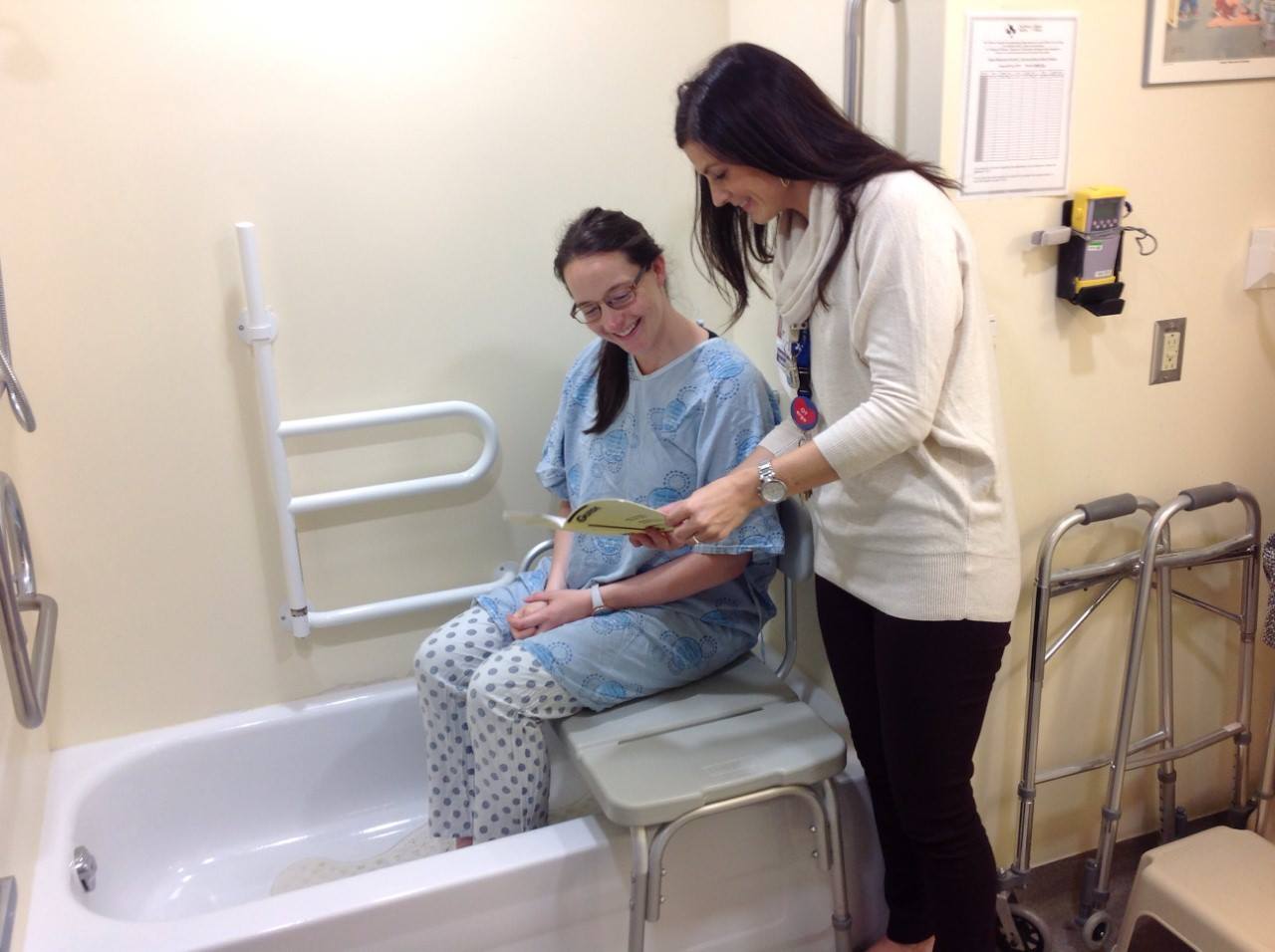 Patient sits on stool in bathtub as health care provider reads to them from a booklet